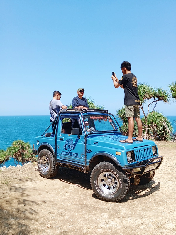 Timang Shuttle jeep located in Timang beach area. Two passengers stand up in the rear seat. The jeep driver took a photo of the passengers from the machine's cap.
