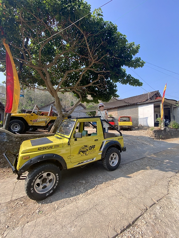 A yellow jeep at the Timang beach parking area is ready to bring passengers. The woman passenger stands up in the rear seat.