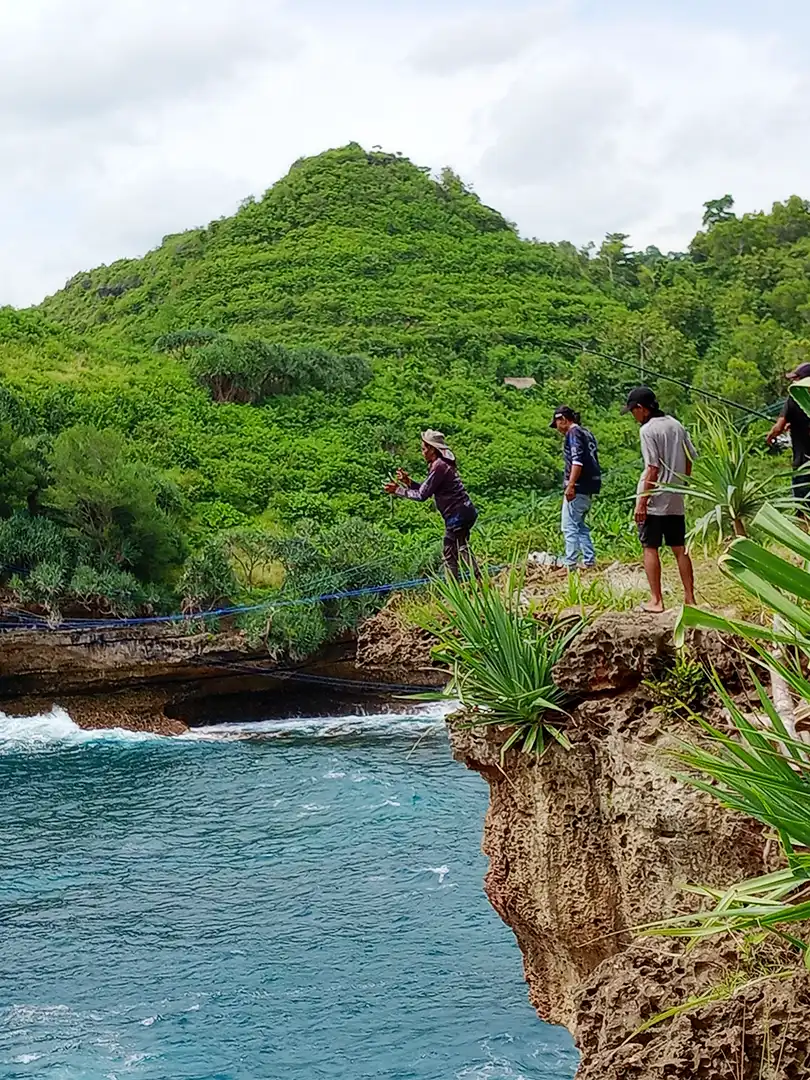 Fishermen fighting to land the fish on the edge of the rock at Timang Beach. One man helped set the hook with the strongest line to lift the fish in a high-risk position at the rock's edge.