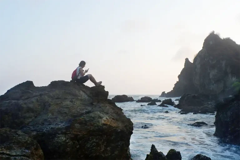 A visitor sitting on the coastal rock at Watulumbung Beach to enjoy the sunset.
